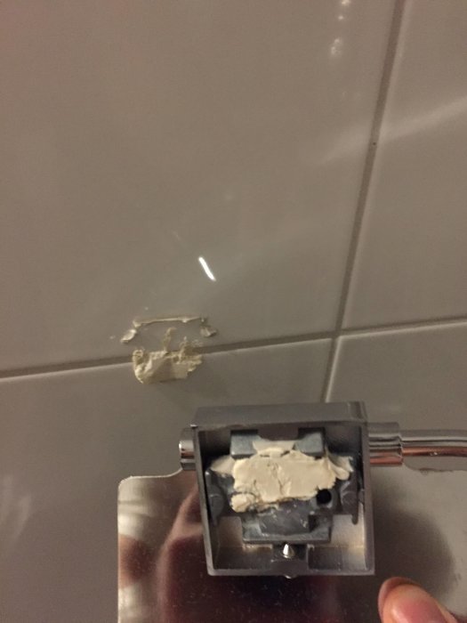 Toarullehållare i mässing lossnad från kakelvägg med synlig epoxy och silikon.