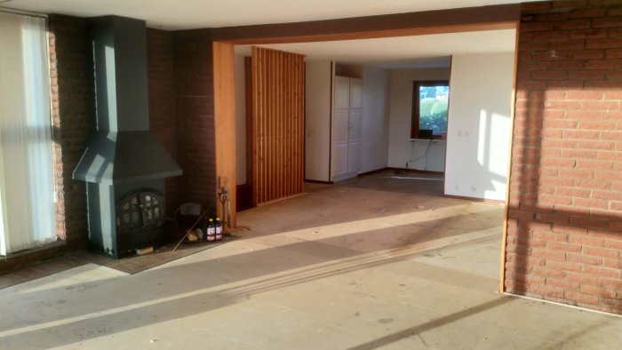 Renoverat vardagsrum med öppen spis och borttaget golv, exponerade tegelväggar och träskiljevägg.