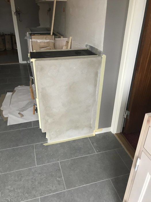Putsad vägg nära spis skyddad med tejp och plast under renovering.