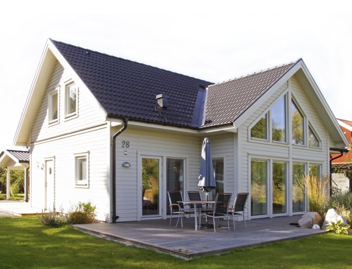 Vit villa från Mälarvillan med blått tak, stora fönster och uteplats.