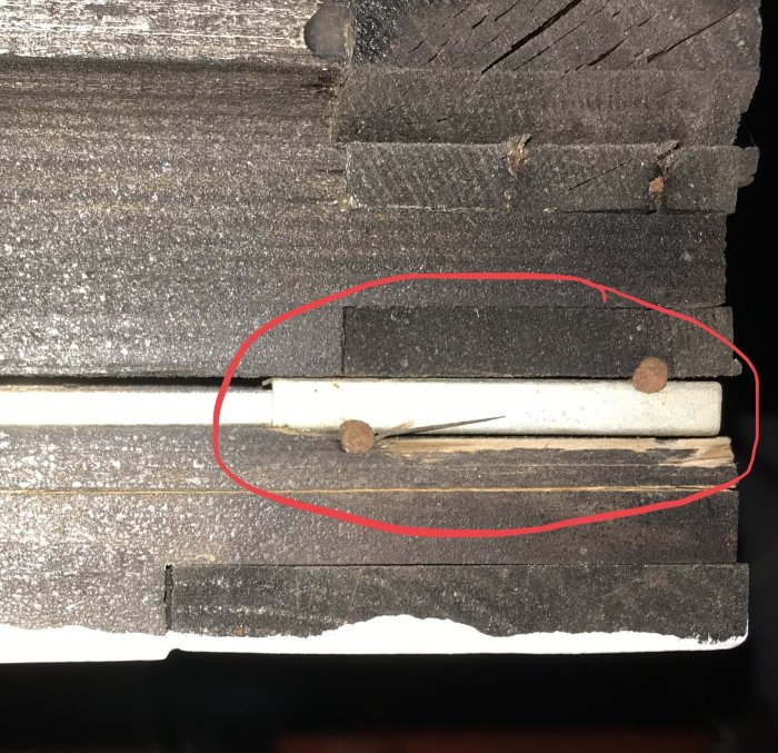 Skadad låsmekanism med en spanjolettarm och plåtbitar vid fönstrets underkant markerade med en röd cirkel.