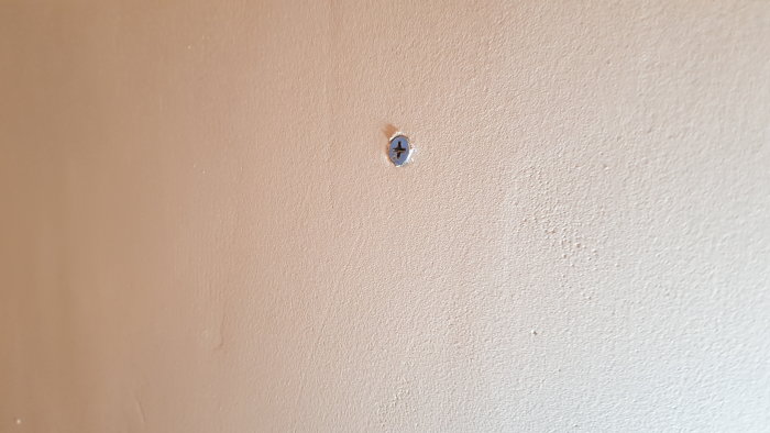Breddspacklad och grundmålad vägg med en skruv för att illustrera väggens stabilitet.