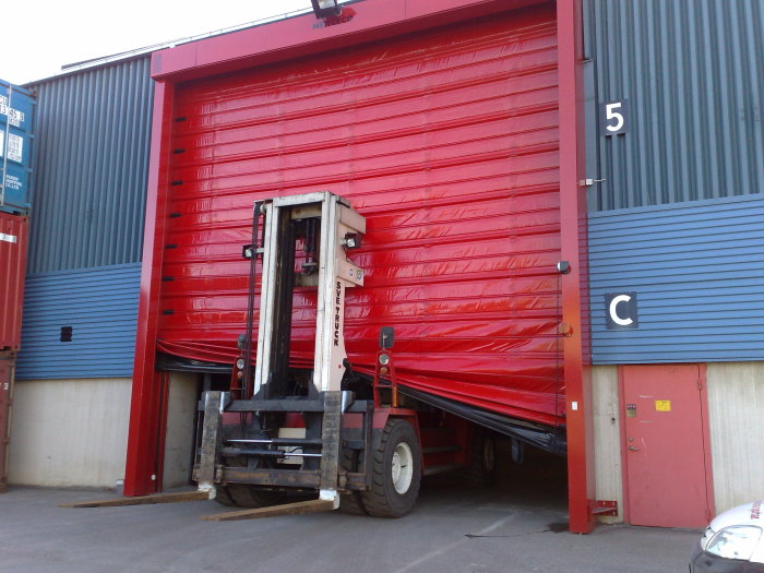 En gaffeltruck som lyfter en röd, ihopdragen industriport.