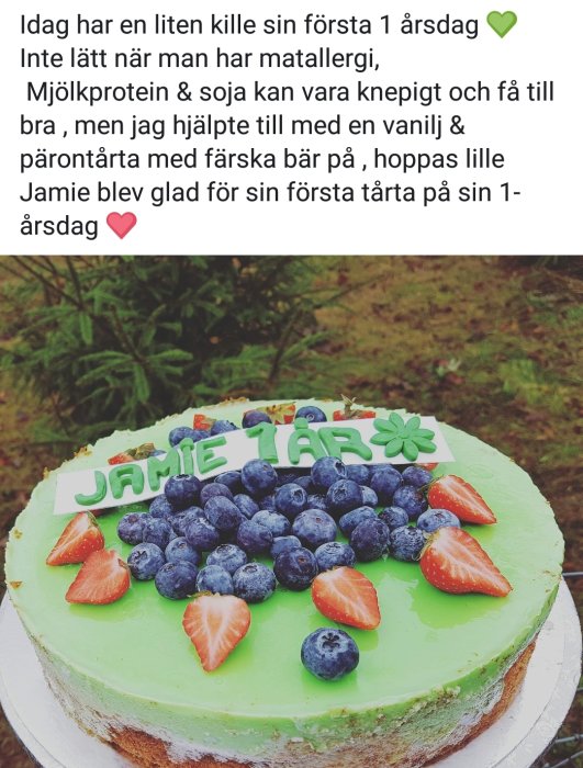 Grön tårta med texten "Jamie 1 år" dekorerad med färska jordgubbar och blåbär.