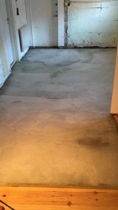 Renoverat rum med nyligen gjuten betonggolv och delvis putsade väggar.