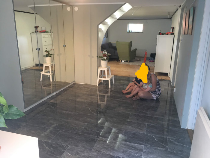 Renoverat vardagsrum med blankt marmorgolv och modern inredning, två personer på golvet.
