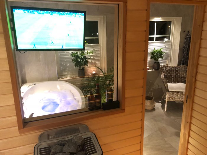 22-tums TV monterad på vägg i bastu med fotbollsmatch på skärmen och syn av angränsande rum.