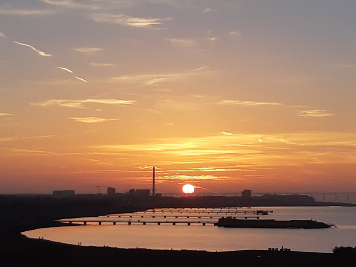 Solnedgång över vattnet vid Ribersborg med silhuetter av pirer och byggnader.