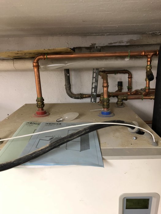 VVS-installation med kopparledningar och ventiler under tak, med en termostat vid väggen.