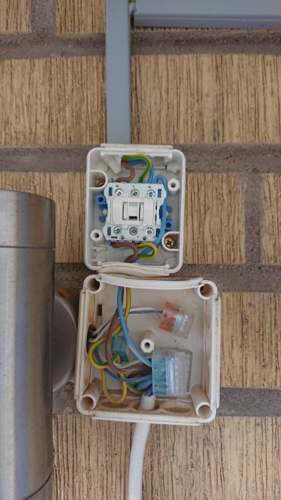 En öppen kopplingsdosa med eluttag, vridströmbrytare och förgrenade kablar på en husvägg.