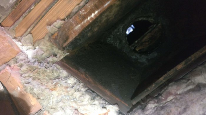 Öppning med sot och isolering där en gammal kamin tidigare suttit, redo för renovering och kamininstallation.