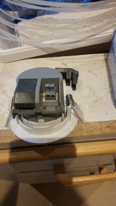 Grå eluttagdelar och fjädrar upplagda på en smutsig yta under renovering.