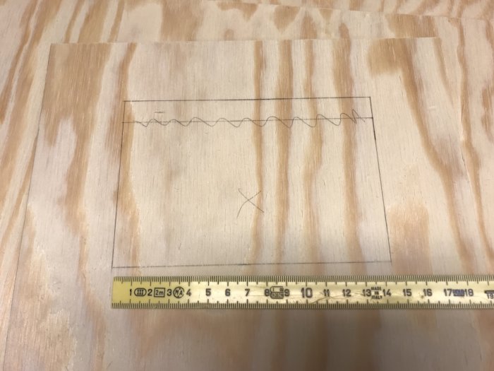 Plywood med utsågade bitar och inritade fönster och dörrar bredvid en tumstock.