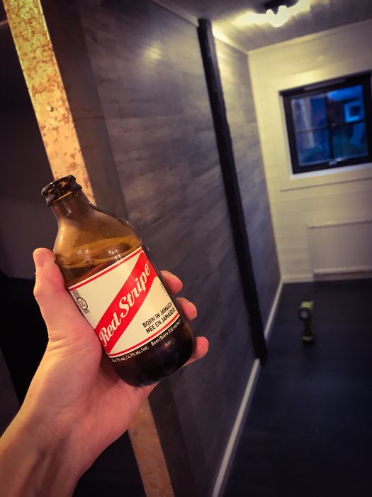 Hand håller ölflaska framför nyinstallerad metallplåt i renoverat rum med fokus på vätskebalans.