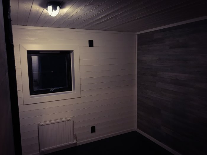 Nyligen renoverat gästrum med vitmålade väggar, taklampa, mörkt laminatgolv och en mörk väggpanel.