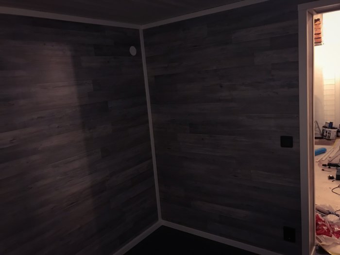 Mörkt träfärgat gästrum med nyinstallerad panel, redo för inredning, med byggmaterial synligt i öppningen.