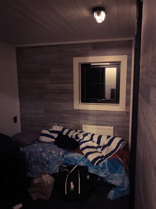 Ett sovrum med träpanel på väggar och innertak, tältsäng beklädd med blått och vitt täcke, väskor på golvet.