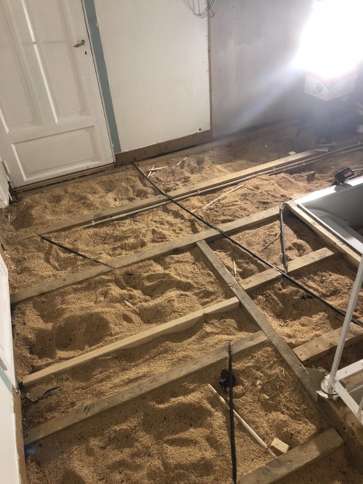 Renoveringsarbete på hallgolv med exponerade golvbjälkar och nylagda el- och nätverksrör.