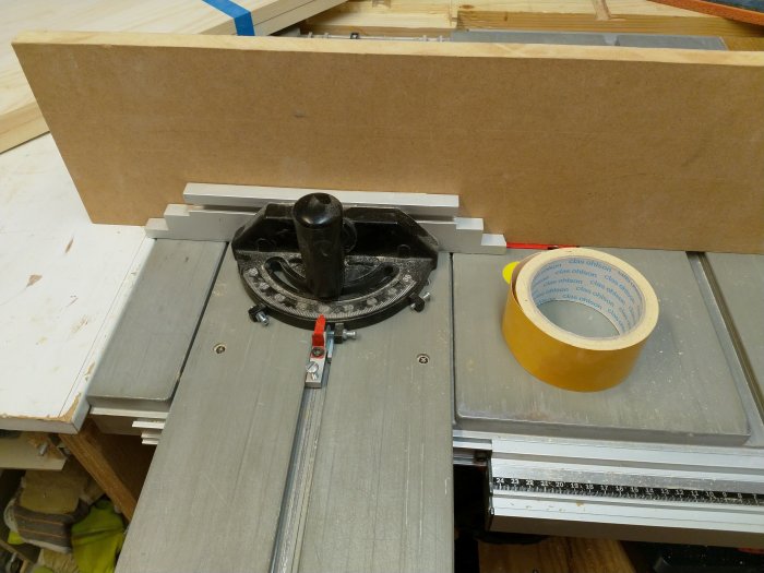 En MDF-skiva fasttejpad på skjutanhållet av en bordssåg, förinställd för att skapa laxstjärtar i träarbetsprojekt.