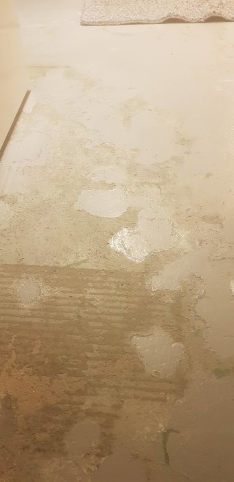 Betonggolv med flagnande grå färg som avslöjar underliggande gammal grön färg, oisolerat.
