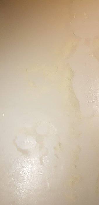 Närbild på ett oisolerat betonggolv med gammal grön färg synlig under nuvarande grått lager.