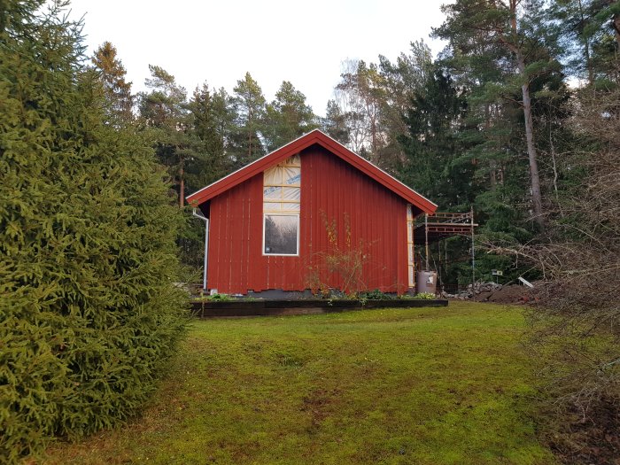 Rödmålad stuga med nyinstallerade fönsterbleck och foder, synlig lockläkt, ställningsdelar vid gaveln.