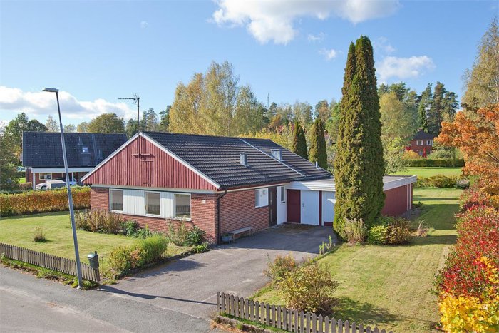 Ett rött tegelhus med separat garage och en trädgård under solig himmel.