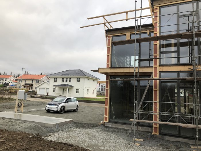 Halvfärdigt hus med plåttak, ställningar och en bil framför en betonggrund för terrass.