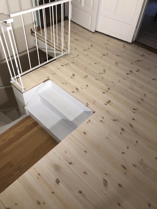 Nyinstallerat ljust trägolv med vit trappräcke och öppen dörr i bakgrunden.