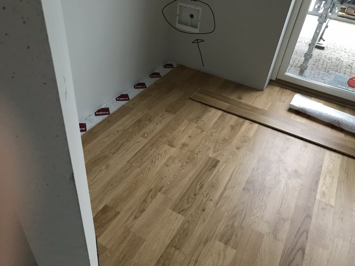Hörn av ett rum med parkettgolv, vit vägg och synligt eluttag, planering för garderobsinstallation.