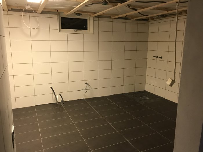 Renoverat källarrum under konstruktion med nylagda klinkergolv och kaklade väggar, kablar för elinstallation synliga.