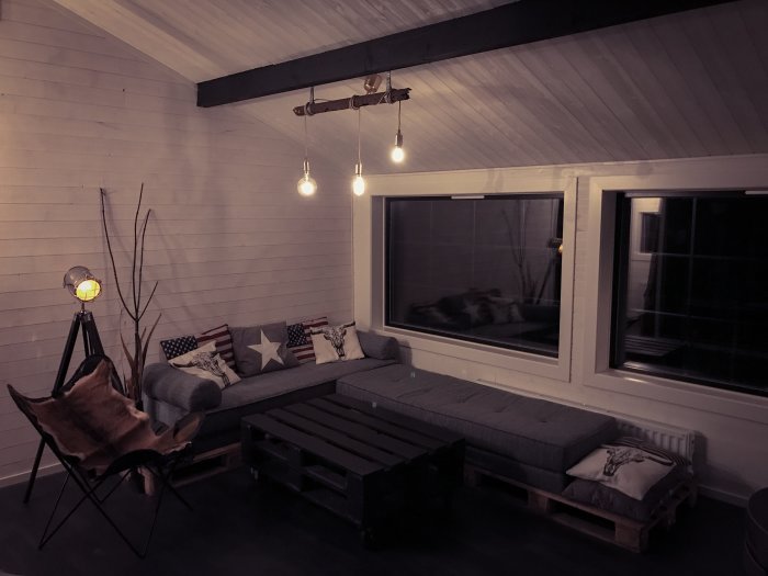 Ett mysigt inrett vardagsrum med fladdermusfåtölj, soffa och USA-inspirerade kuddar, industriell belysning.
