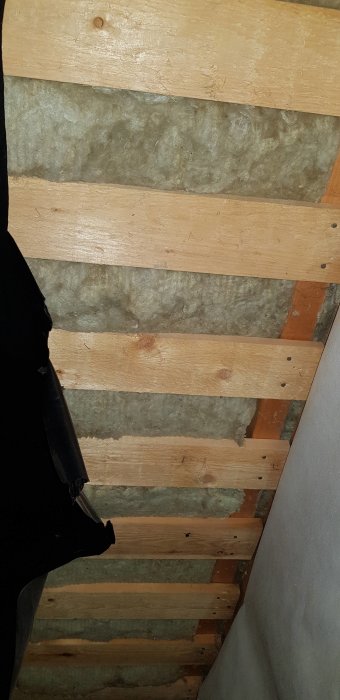 Träreglar och isolering i ett öppet tak inför installation av downlights, med synlig golvisolering och träbrädor.