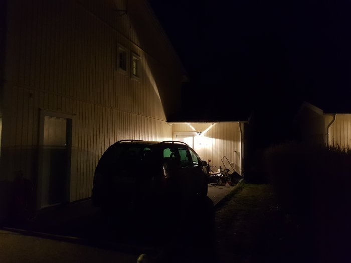 Kvällsbild av ett bostadsrättsparhus med synligt kallförråd och parkerad bil.