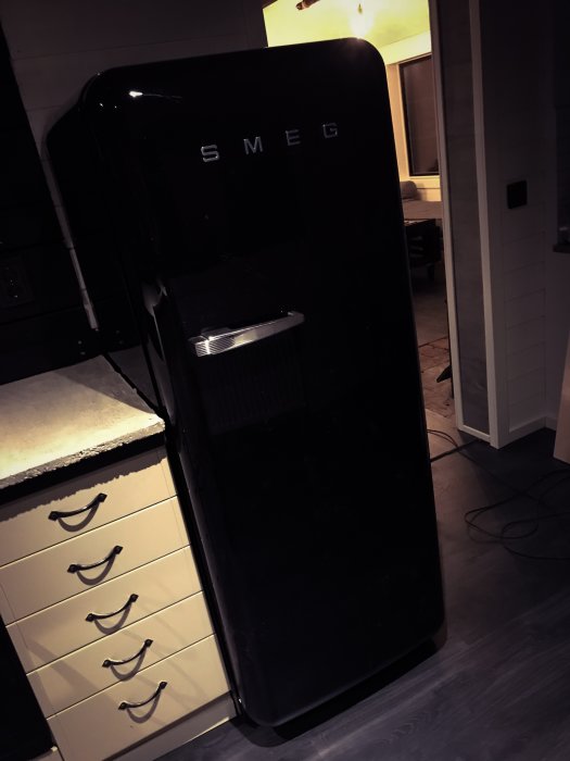 Svart retrostil SMEG-kylskåp i ett delvis renoverat kök med ljusa skåpluckor.