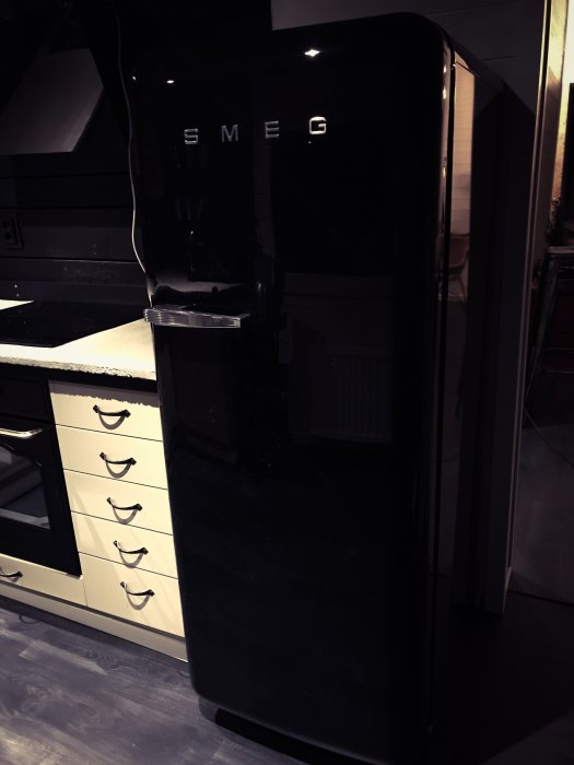 Svart SMEG-kylskåp i ett kök med ljusa skåpluckor och bänkskiva.