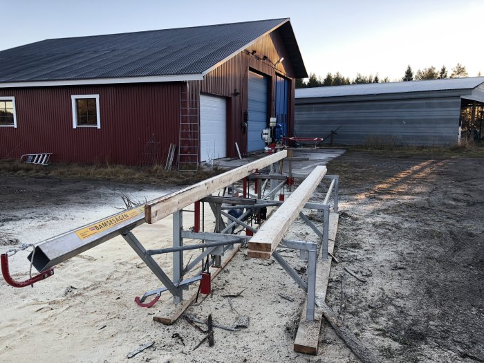 Stor sågutrustning framför byggnader med texten "BAMSESÅGEN", avsedd för bearbetning av långa stockar.