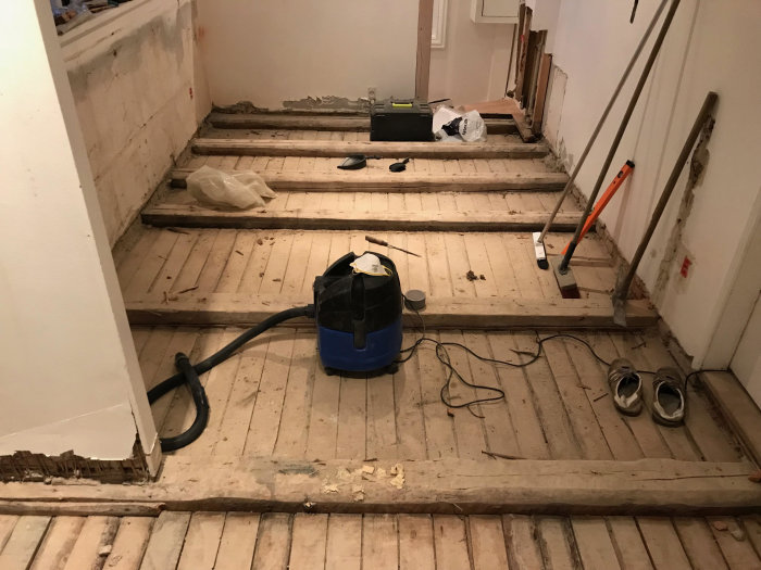 Rum under renovering med synliga golvbjälkar, dammsugare och byggutrustning.