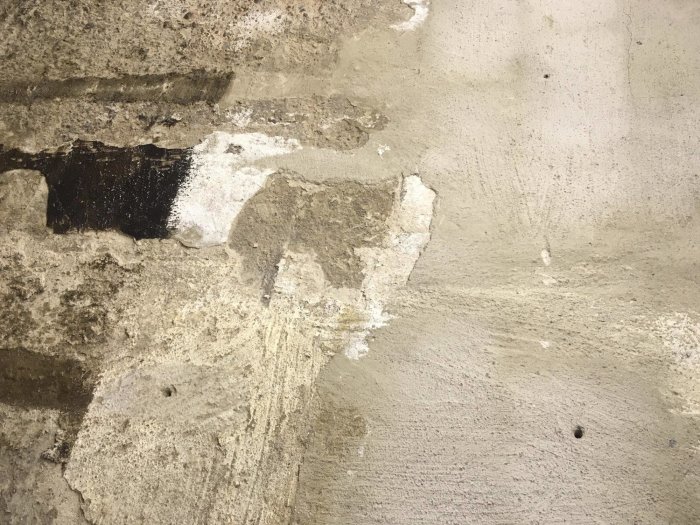 Gamla putsen som lossnar från betongväggen i ett hus byggt 1910, några fläckar med kvarvarande ytskikt.