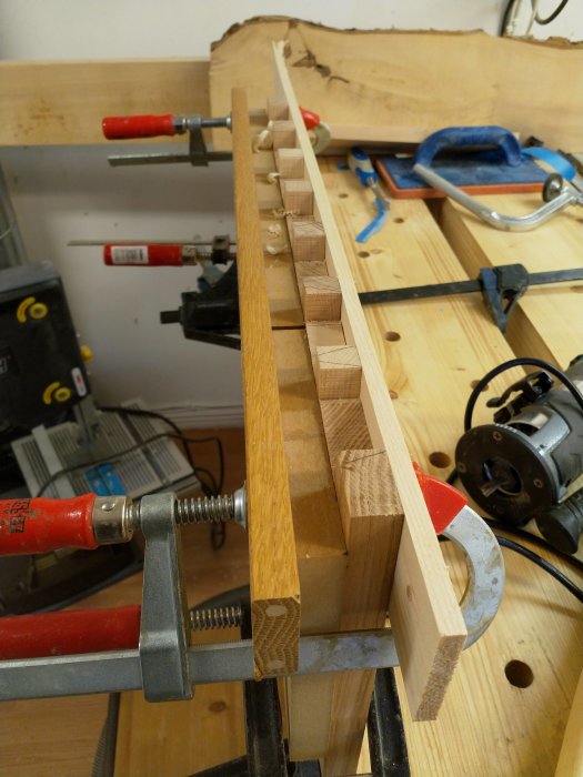 Trästycke fastspänt på arbetsbänk, förberett för snickeri med utmarkerade pinnar och verktyg.
