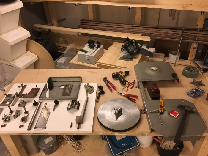 Nedmonterade metalldelar av verktyg spridda på ett arbetsbord i en verkstad med verktyg och material i bakgrunden.