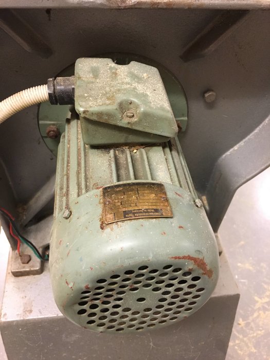 Gammal elektrisk motor med damm och slitage, kabel och märkplåt synlig.