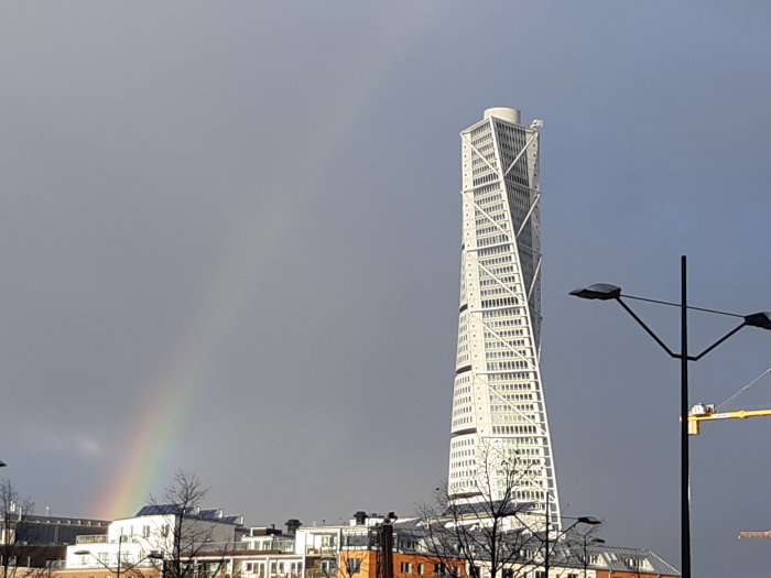 Turning Torso skyskrapa i Malmö med en delvis synlig regnbåge och mörka moln i bakgrunden.