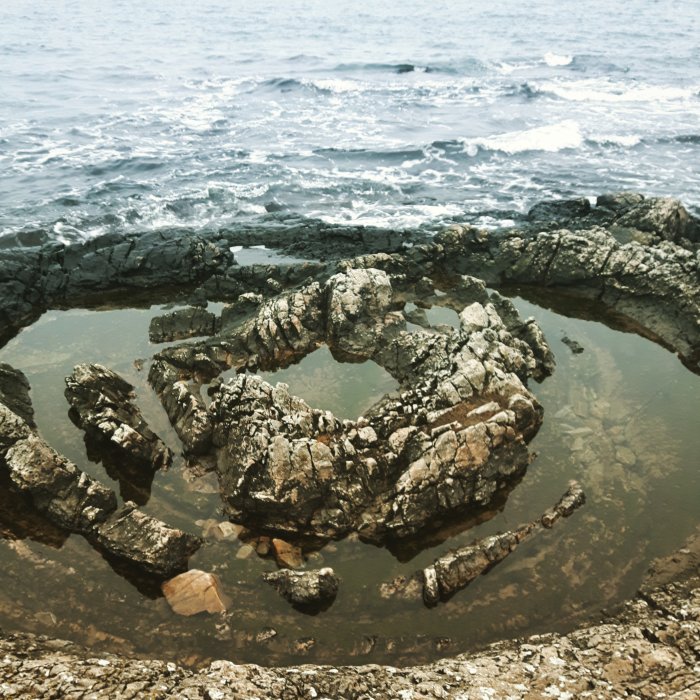 Naturlig stenformation som liknar ett badkar nära havet under en molnig dag.