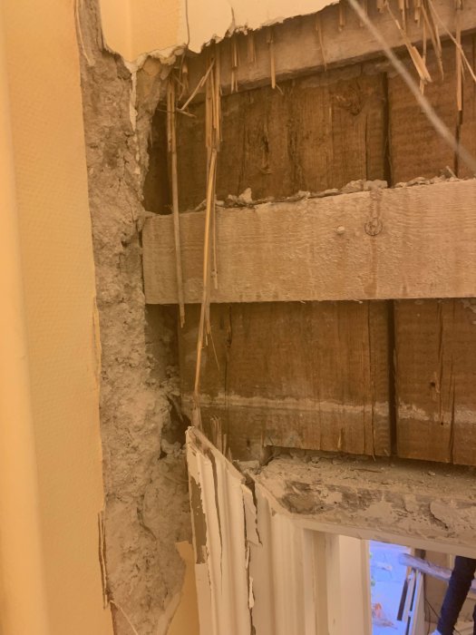 Seinän avauskohta, jossa näkyy puu- ja kipsirakenteita. Vaurioituneita kipsilevykerroksia ja puupalikka tukee rakenteita alapuolella.