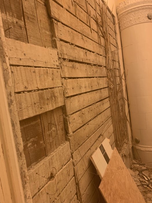 Vanha seinä puusta ja kipsistä keskellä purkuprosessia, oikealla näkyy kakluuni.