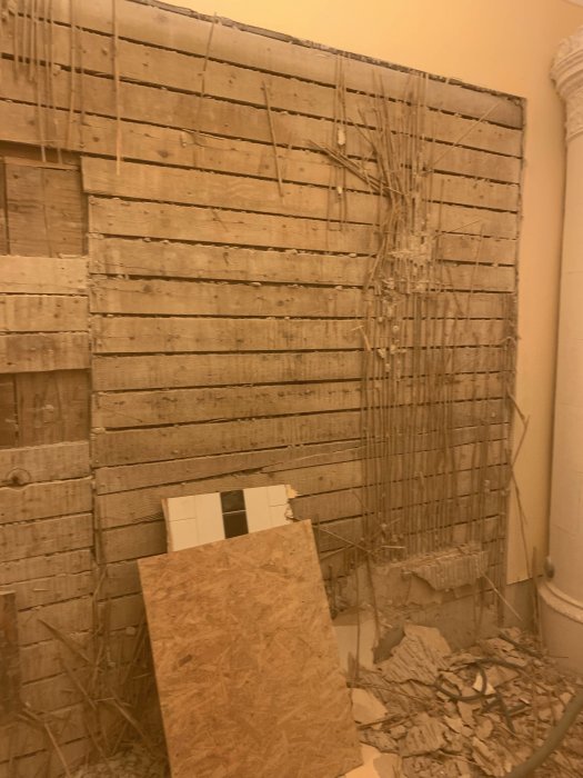 Seinän purkutyö, jossa paljastuu puiset laudoitukset ja sähköjohtoja. Edessä on vaneria ja lattialla romua ja purkujätettä.