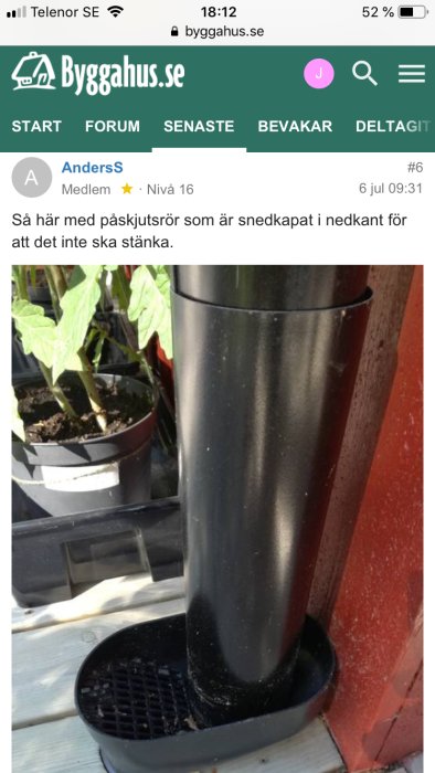 Svart stuprör med påskjutsrör nära husvägg som leder ner i avrinningsbrunn, bredvid växter i krukor.