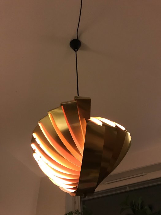Taklampa med spiralformade metallskivor och skinande ljus mot en vit vägg.