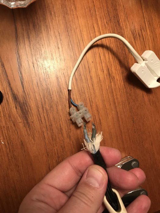 En hand håller en strömkabel med exponerade trådar kopplade till en sockerbit och en vit kontakt.